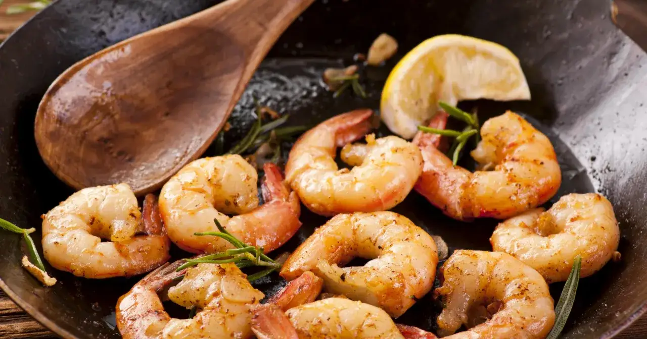 Soczyste krewetki z grilla, przyprawione ziołami i podane z cytryną, kuszą apetycznym wyglądem. Drewniana łyżka sugeruje, że danie jest gotowe do podania.