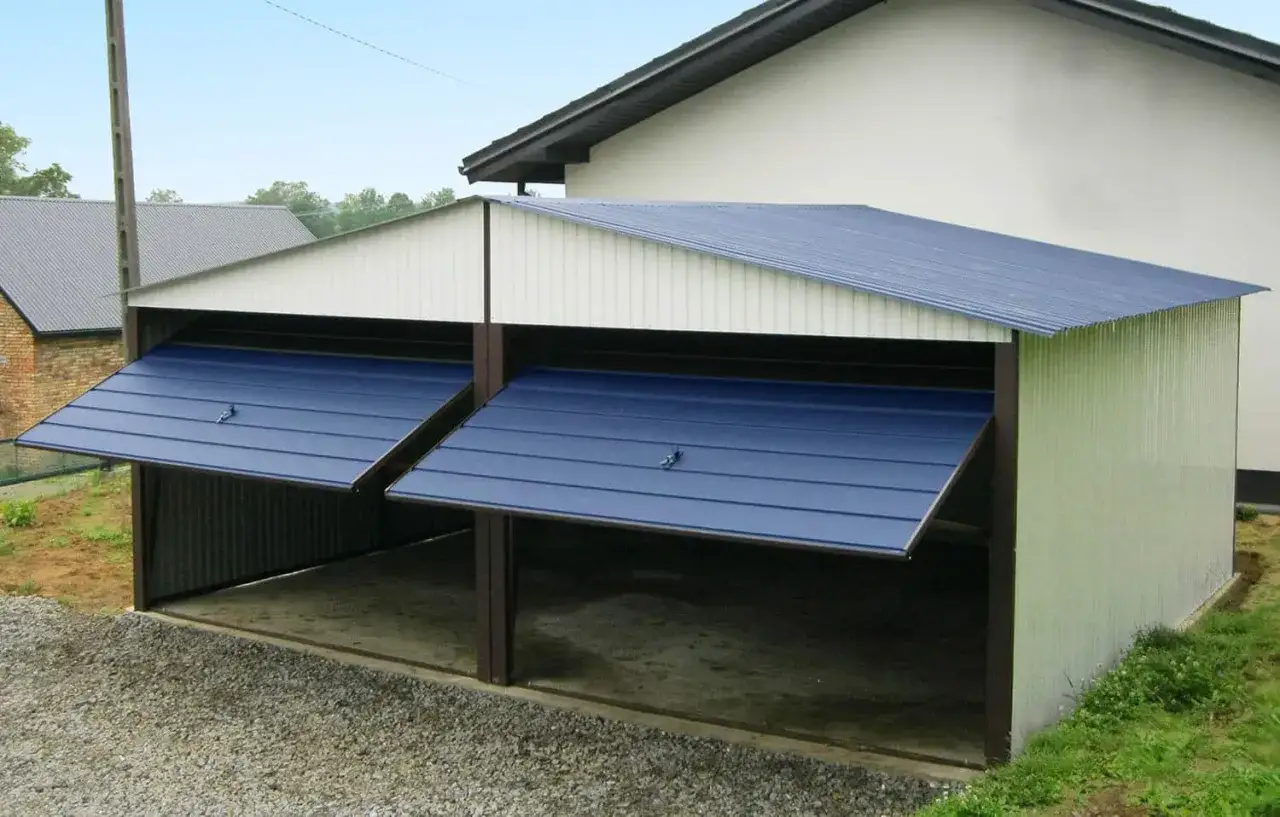 Nowy garaż dwustanowiskowy obok domu, z niebieskimi, uchylnymi bramami. Świetny pomysł na garaż obok domu, zapewniający ochronę pojazdom.