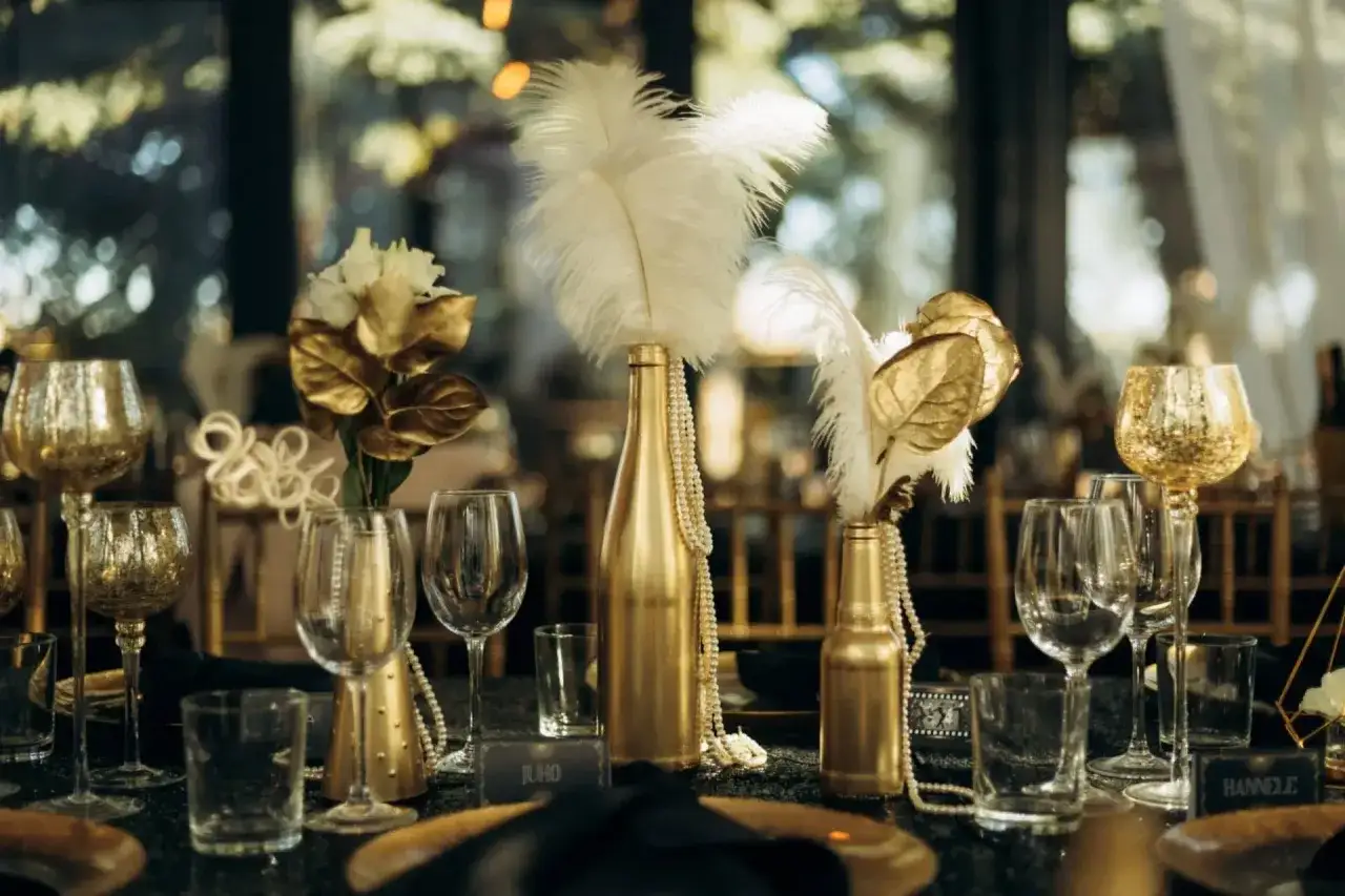Złote kieliszki, pióra i perły podkreślają różnicę między weselem w stylu glamour a nowoczesnym minimalizmem.