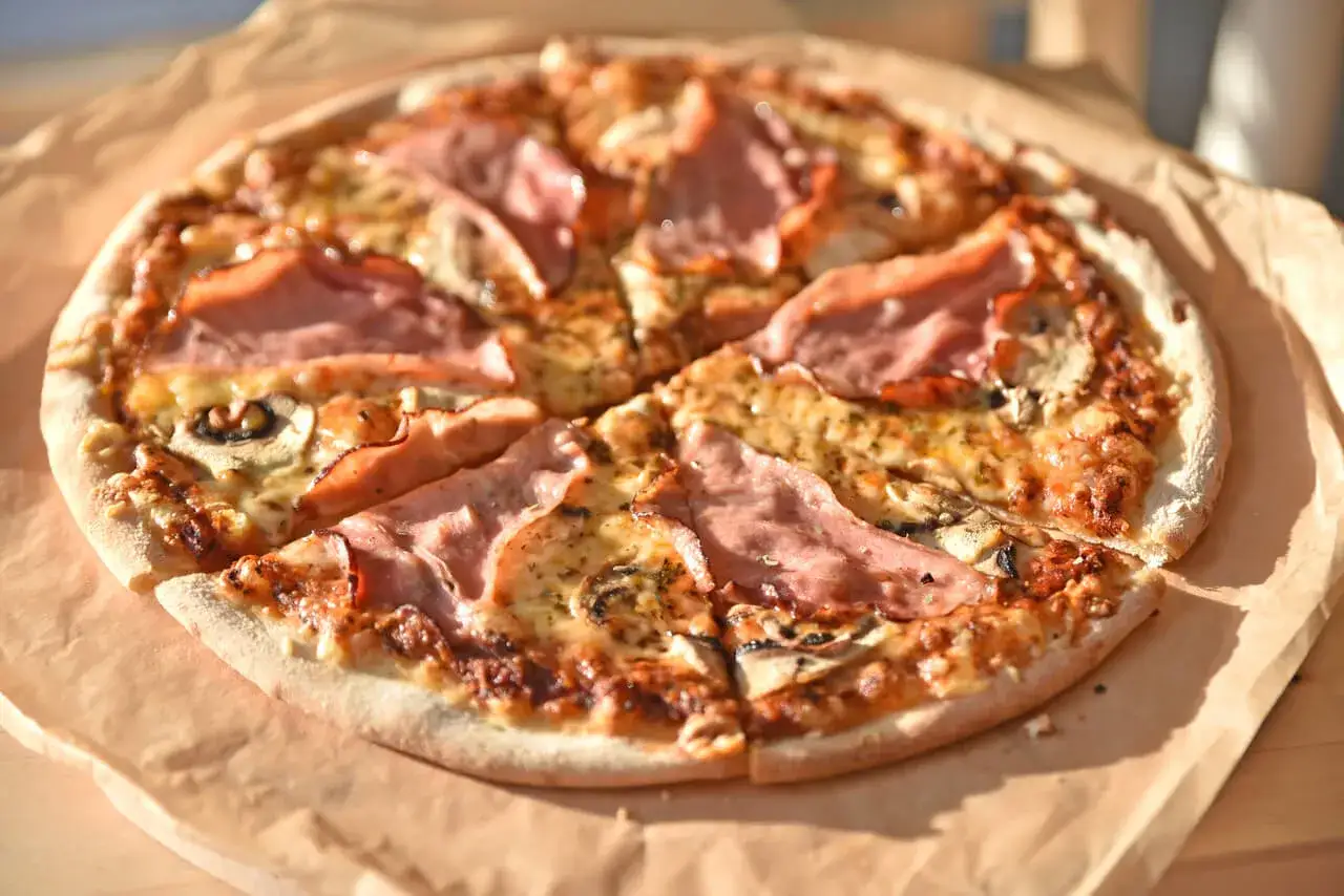 Pizza z szynką i pieczarkami do pizzy, pachnąca i apetyczna, gotowa do podania.