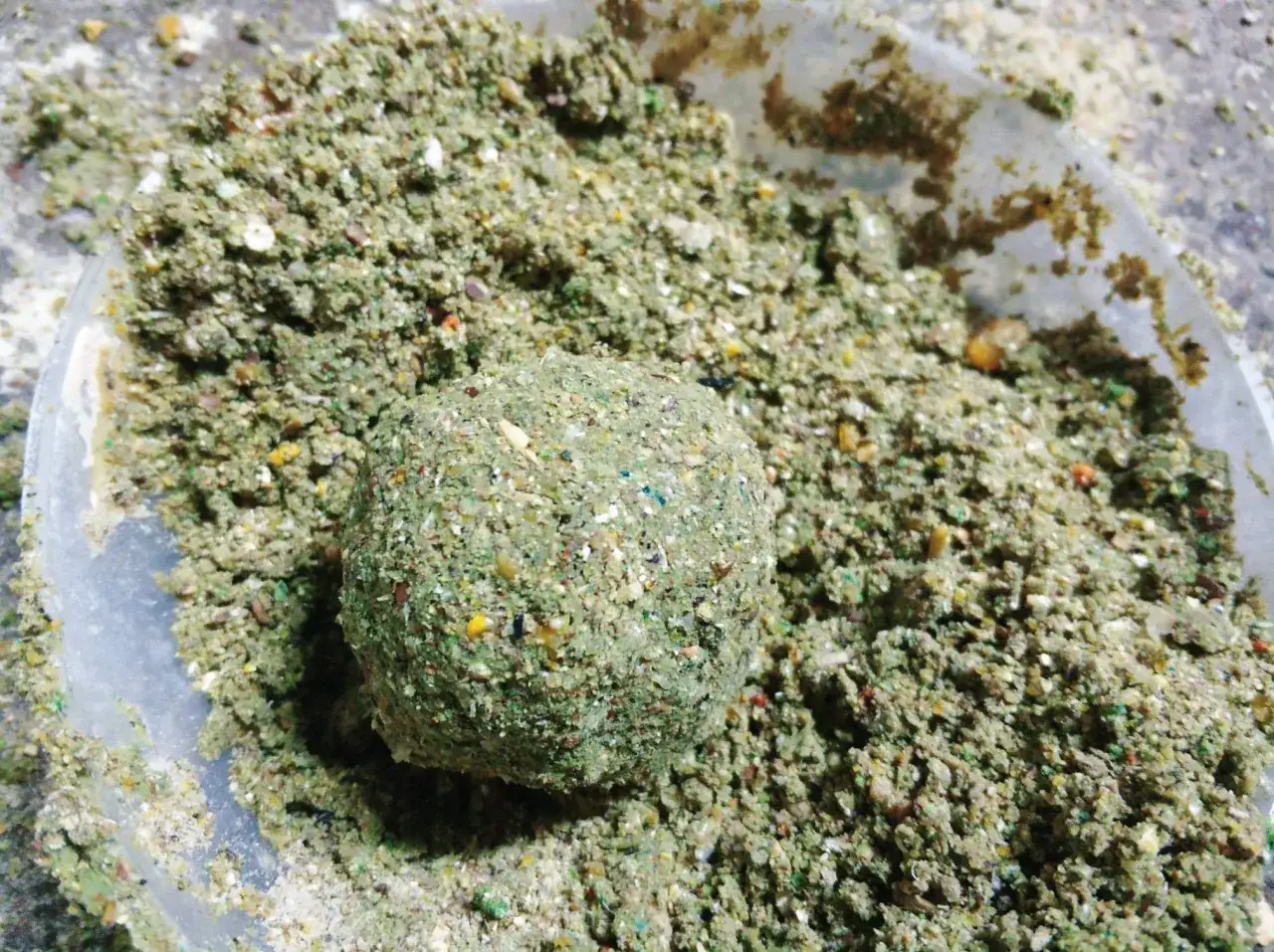 Domowa zanęta na lina, kulka z mieszanki ziaren i ziół w plastikowym pojemniku.