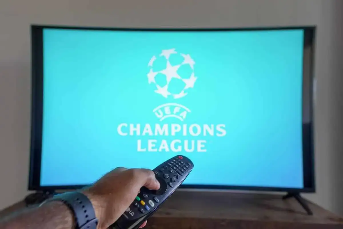 Ręka z pilotem gotowa do włączenia transmisji. Gdzie oglądać Ligę Mistrzów? Na ekranie logo UEFA Champions League.
