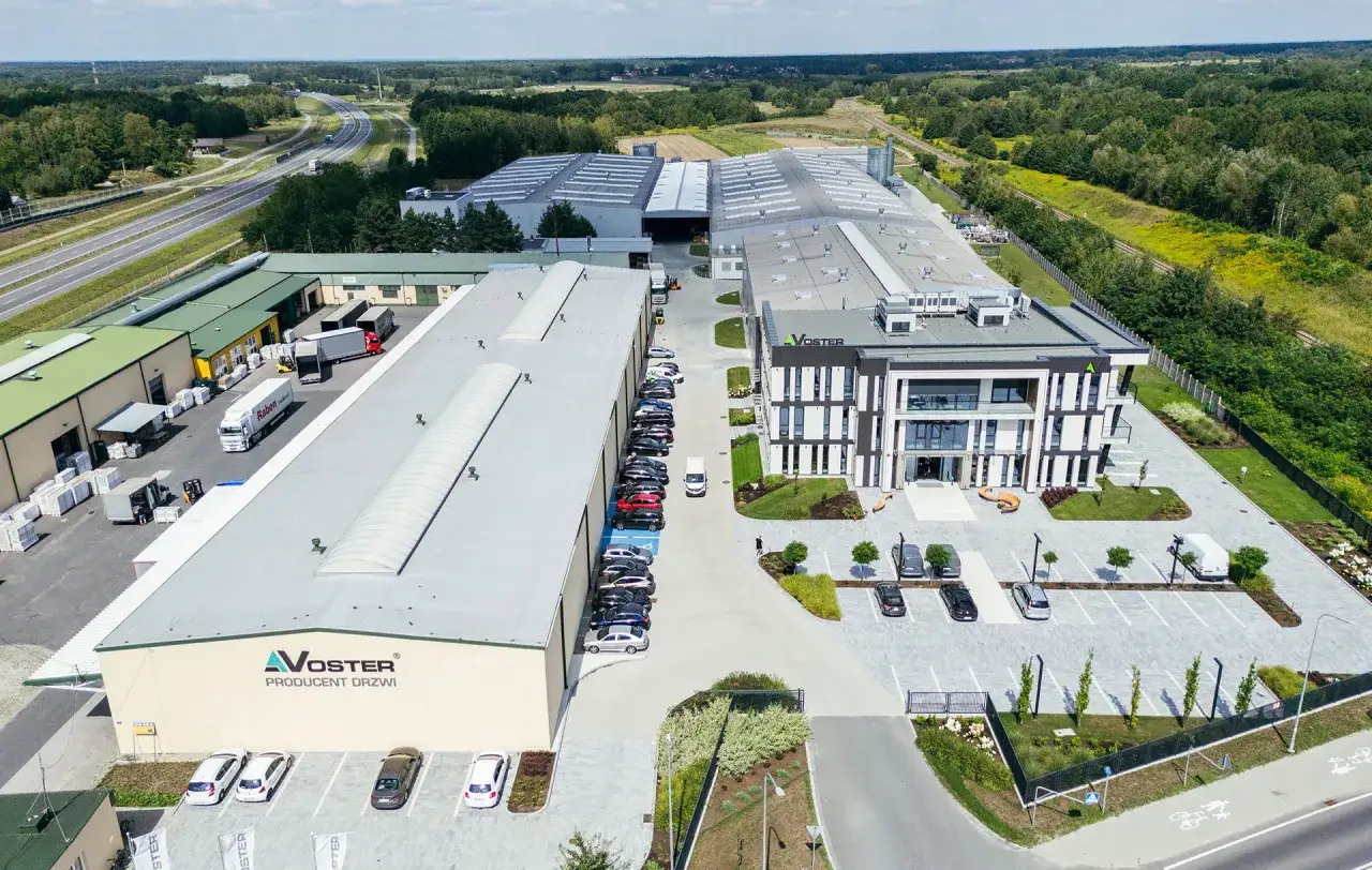 Nowoczesny kompleks produkcyjny Voster producent drzwi, z drogą szybkiego ruchu w tle.