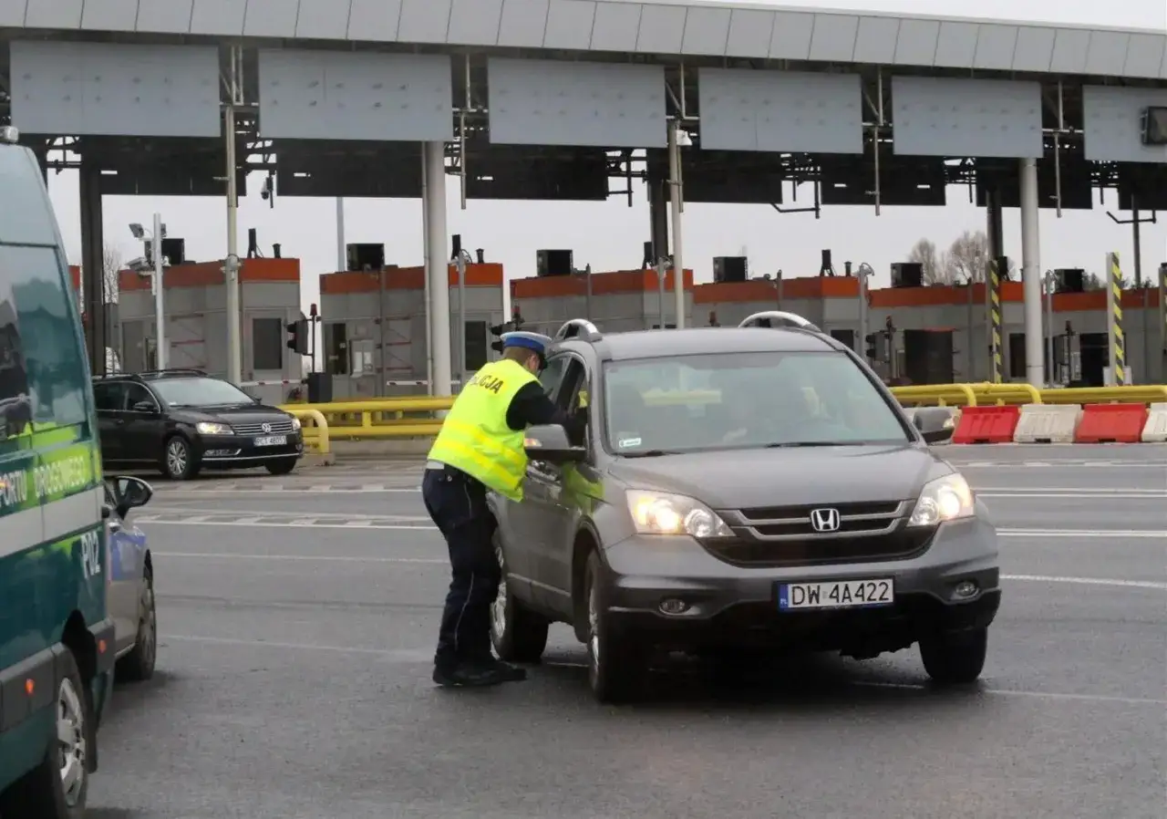 Policjant w kamizelce odblaskowej rozmawia z kierowcą przy bramkach. Czy autostrada A4 jest płatna? Tak, w tym miejscu pobierane są opłaty.
