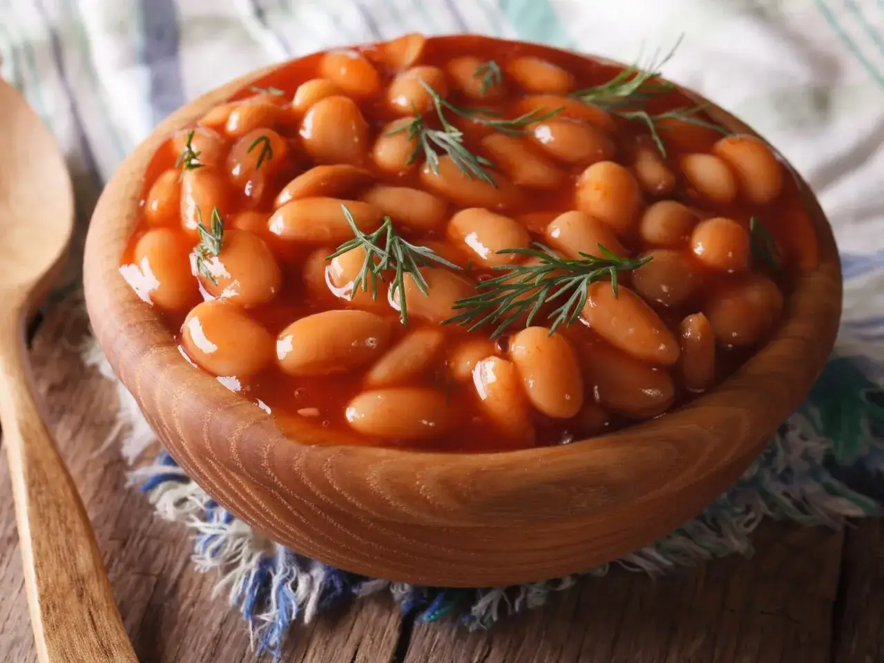 Fasola po bretońsku w drewnianej misce, ozdobiona koperkiem. Idealne przyprawy do fasoli po bretońsku to majeranek i tymianek.