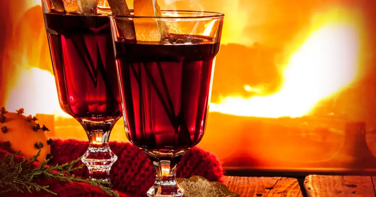 Dwa kieliszki gorącego grzańca z pomarańczą i cynamonem na tle płonącego kominka.