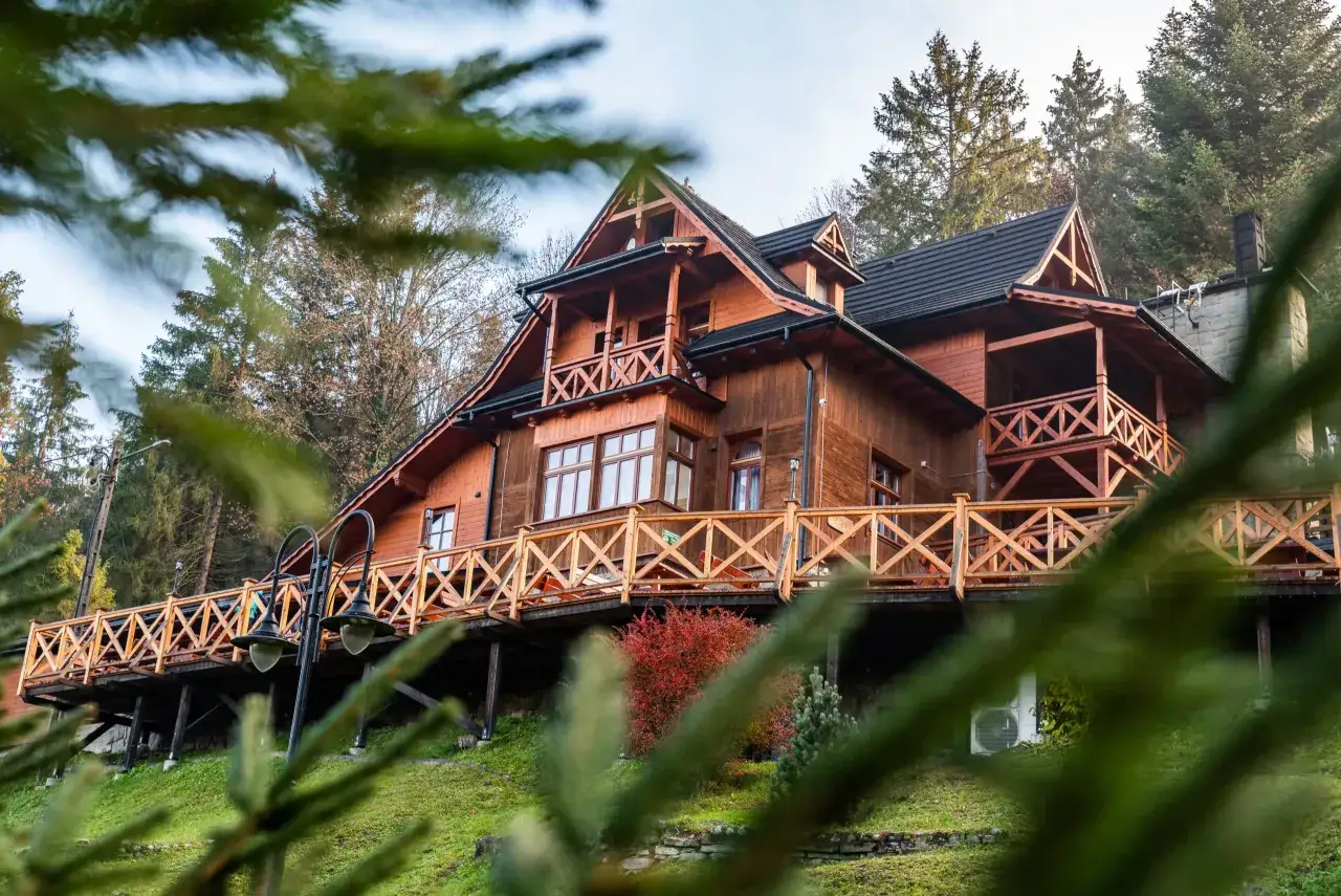 Drewniane schronisko turystyczne z tarasem i balustradą, otoczone drzewami.