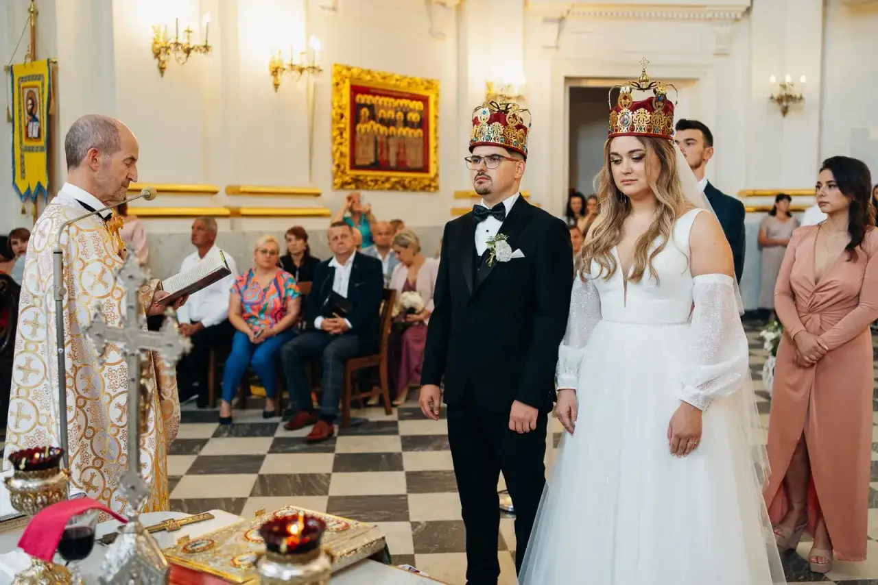 Uroczystość zaślubin w cerkwi. Pan młody, niczym ludowy grajek z Ukrainy, w eleganckim czarnym garniturze, z narzeczoną w białej sukni, przyjmują błogosławieństwo.