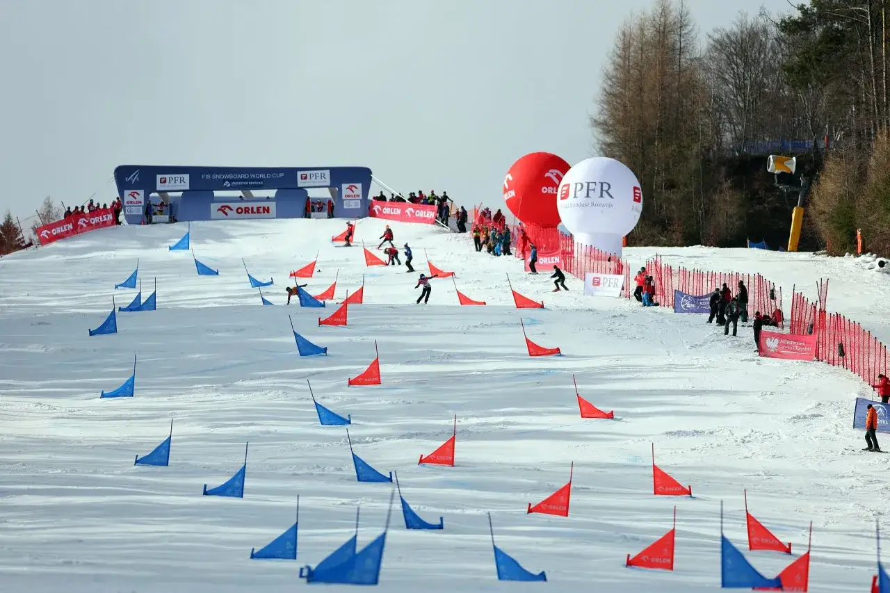 Zawodnicy snowboardu pokonują trasę z czerwonymi i niebieskimi tyczkami na stoku Jaworzyny Krynickiej.
