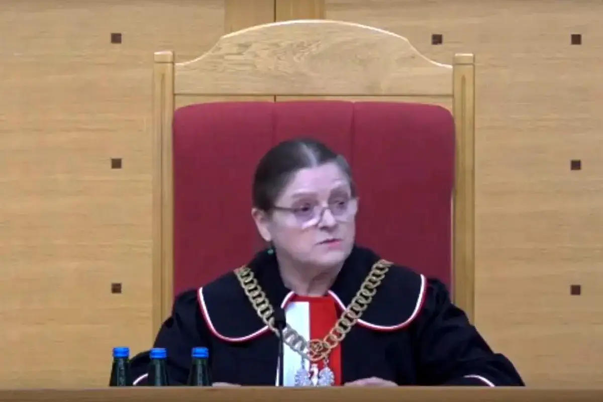 Sędzia w todze i łańcuchu na szyi, siedzi za stołem z butelkami wody. Czy sędziowie płacą składkę zdrowotną?