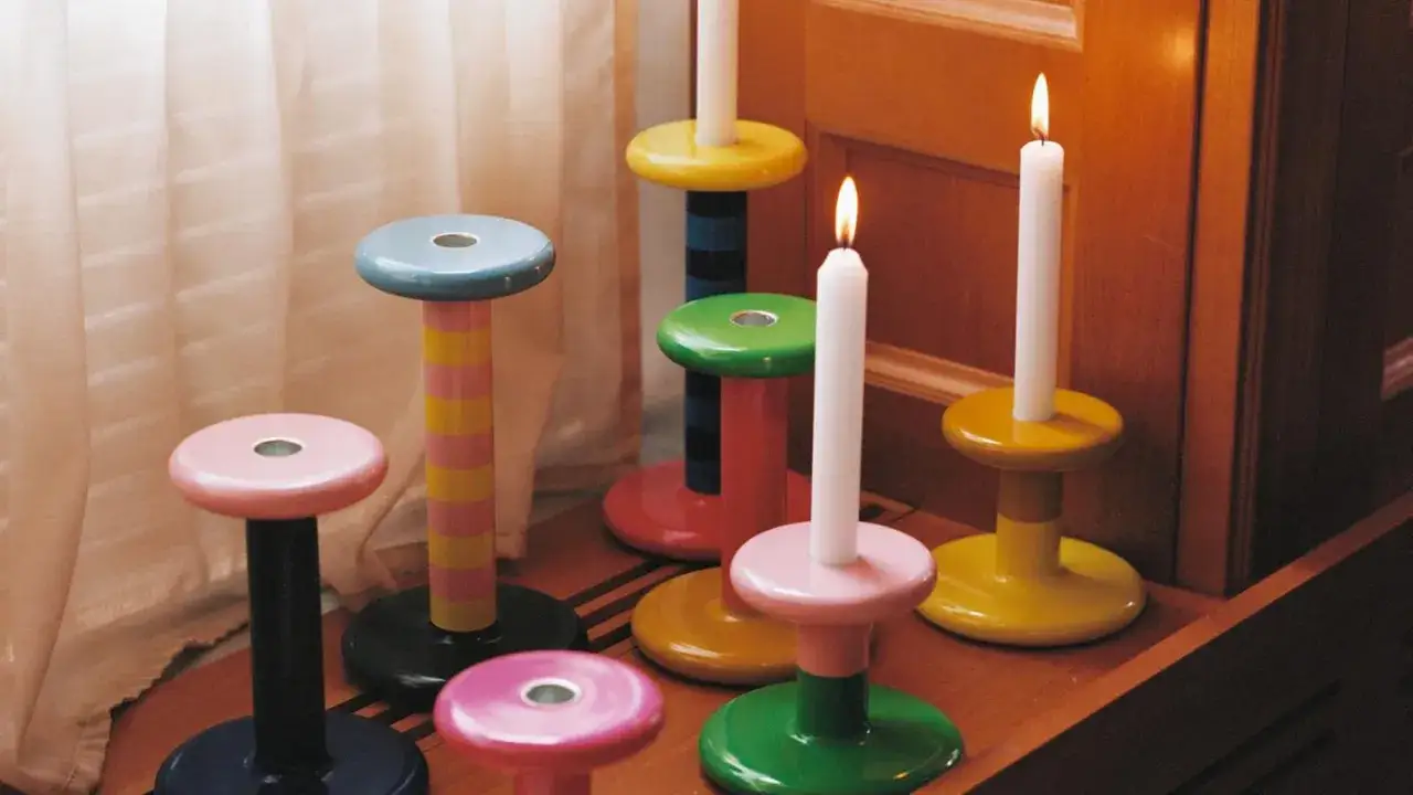 Bunte Kerzenständer in verschiedenen Formen und Farben, einige mit brennenden Kerzen.