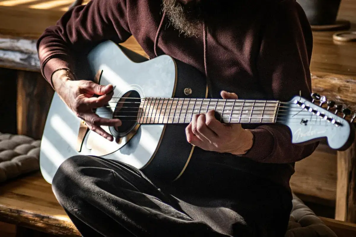 Mann spielt Akustikgitarre, Hände auf Saiten und Plektrum.