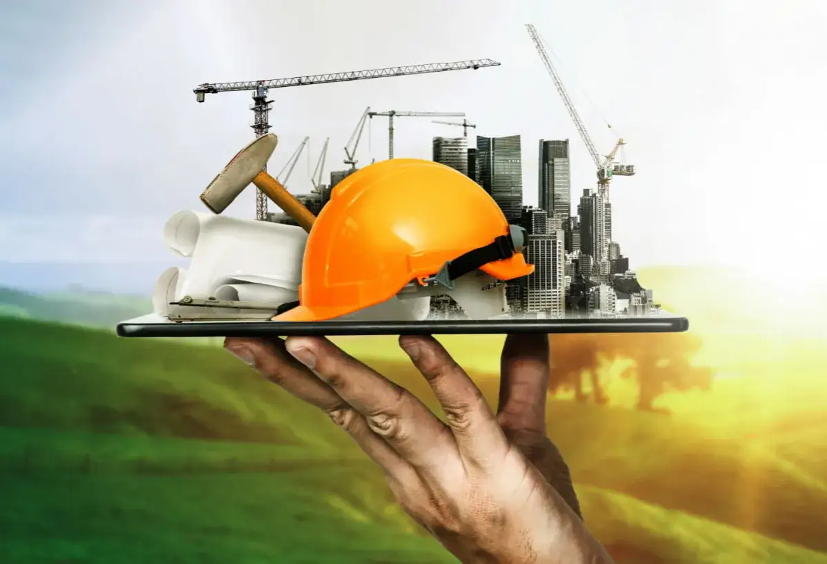 Dłoń trzyma tablet z budowlanymi symbolami: kask, młotek, plany, dźwigi i miasto.