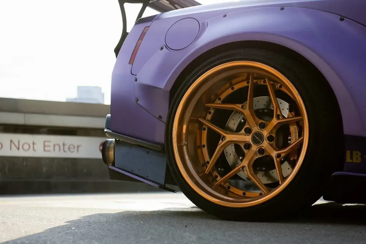 Modyfikacja auta z fioletowym lakierem i złotymi felgami. Zastanawiasz się, ile waży felga aluminiowa? Ta wygląda na solidną!
