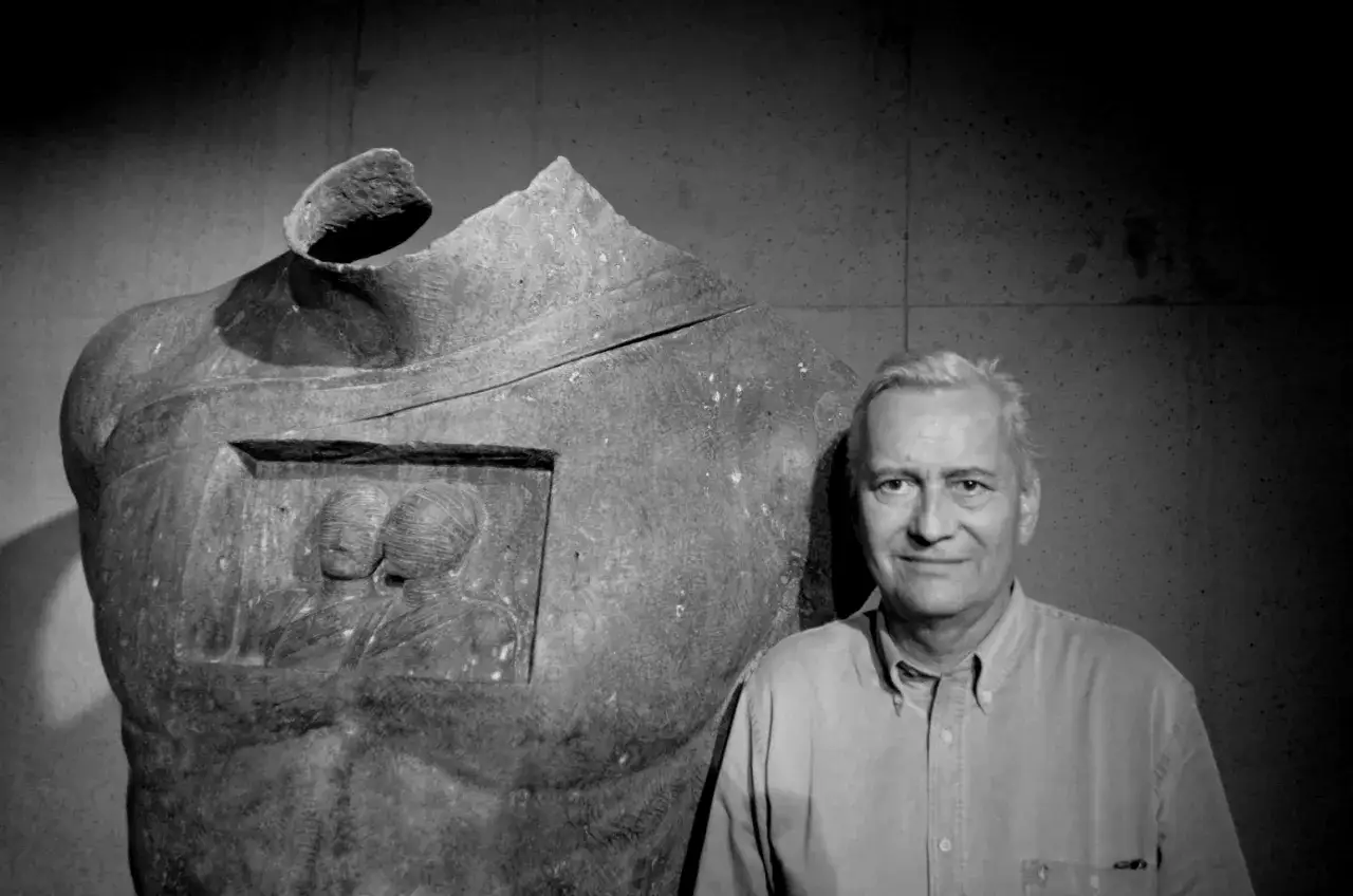 Czarno-białe zdjęcie Igora Mitoraja obok jego rzeźby torsu z pęknięciem.