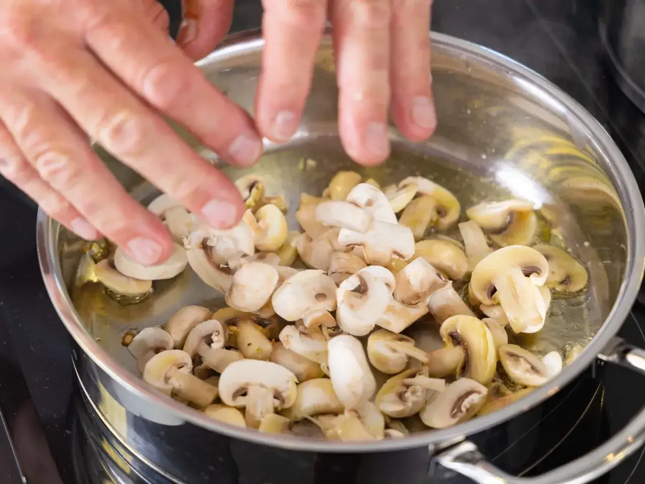 Ręce dodają pieczarki do patelni z rozgrzanym olejem. Smażone pieczarki kcal to pyszny dodatek do wielu dań.