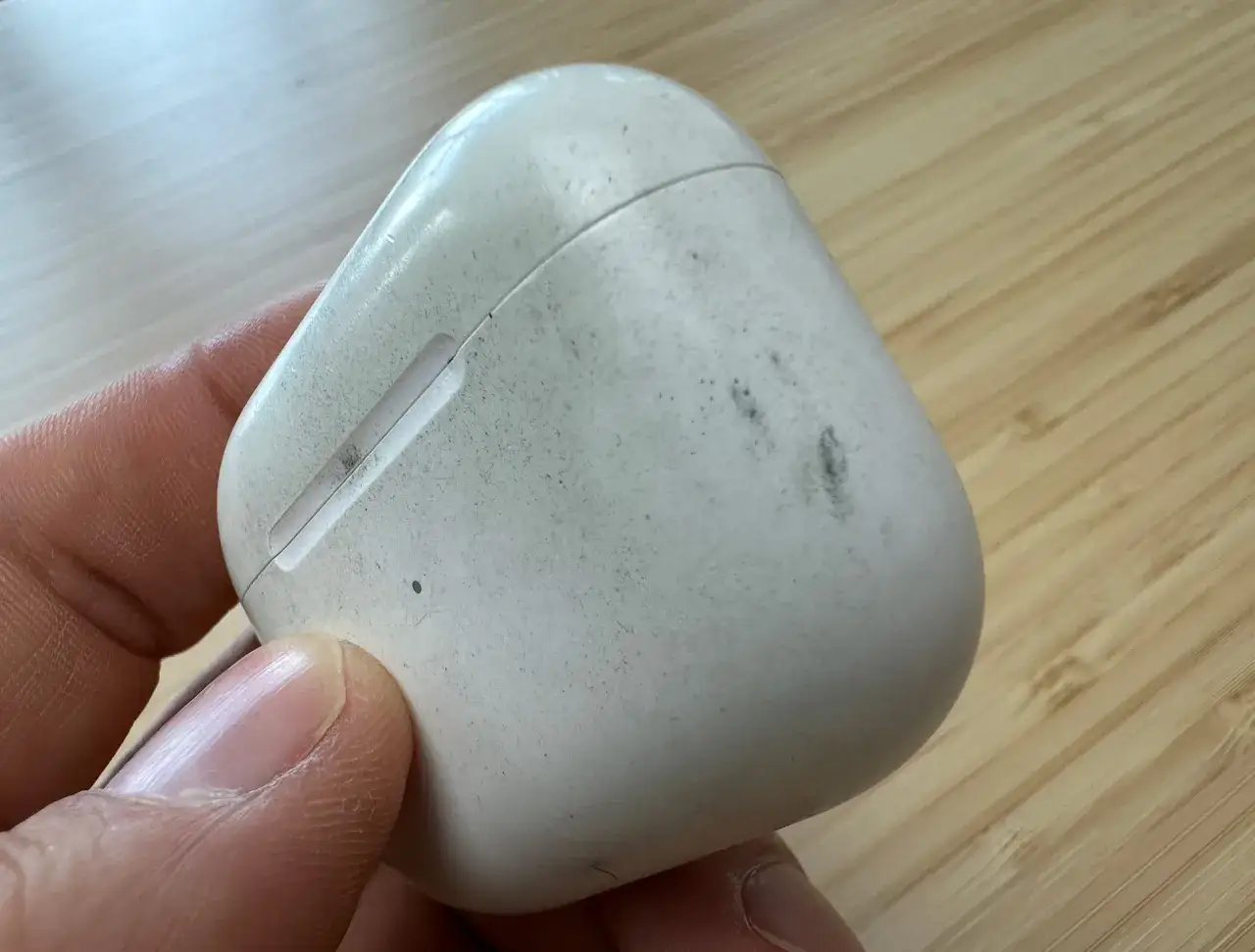 Eine schmutzige weiße Hülle für AirPods wird von einer Hand gehalten.