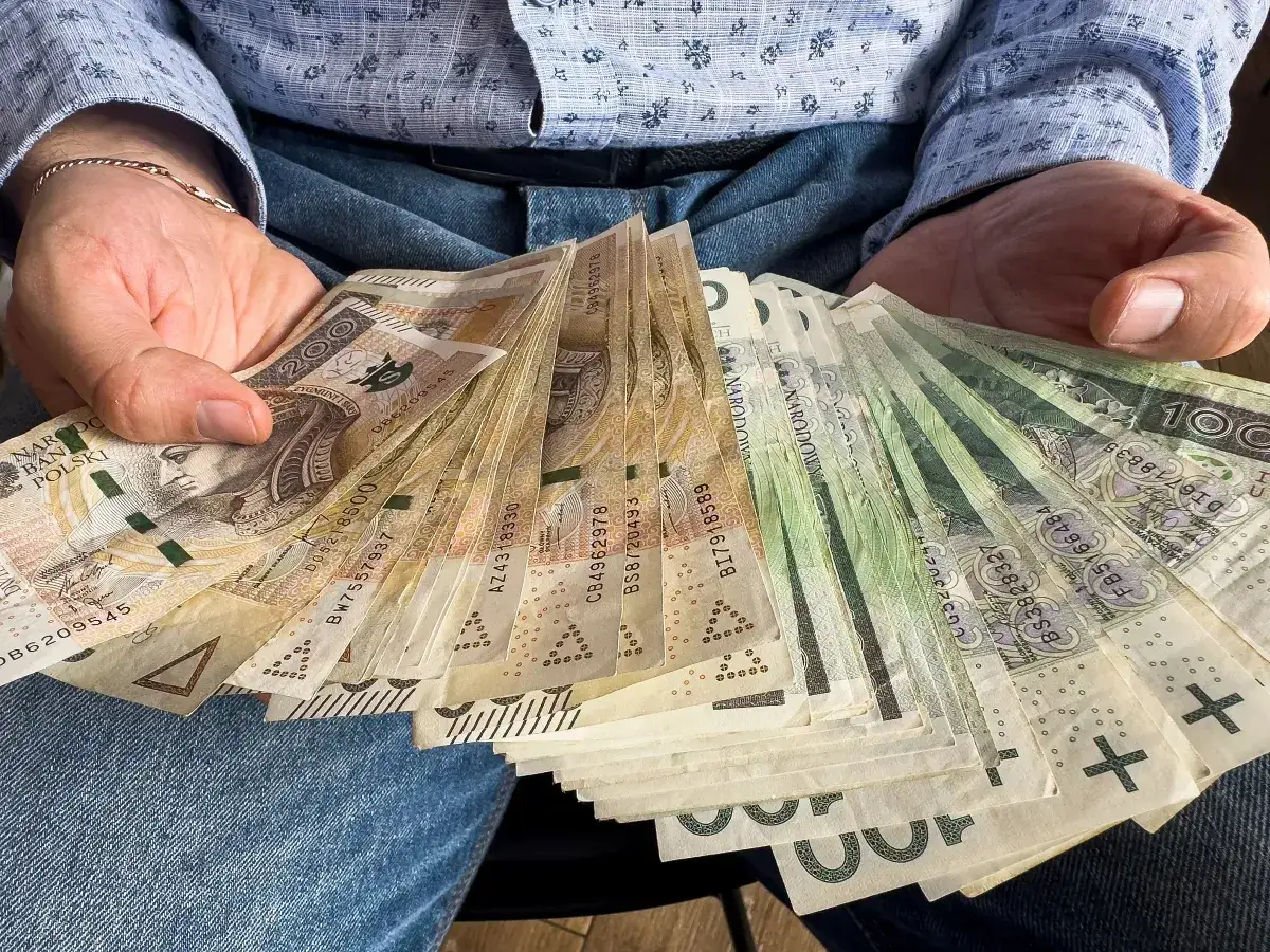 Dłonie trzymające plik polskich banknotów. Czy od pożyczki płaci się podatek? Pieniądze mogą być odpowiedzią.