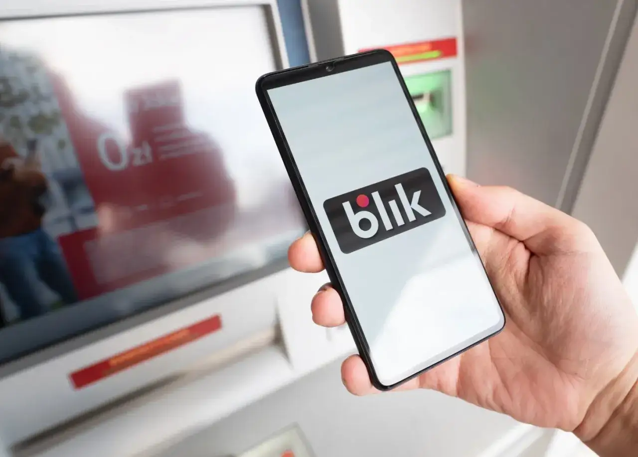 Dłoń trzyma smartfon z logo Blik. Kto wymyślił Blik? To polski system płatności mobilnych, który zrewolucjonizował transakcje.