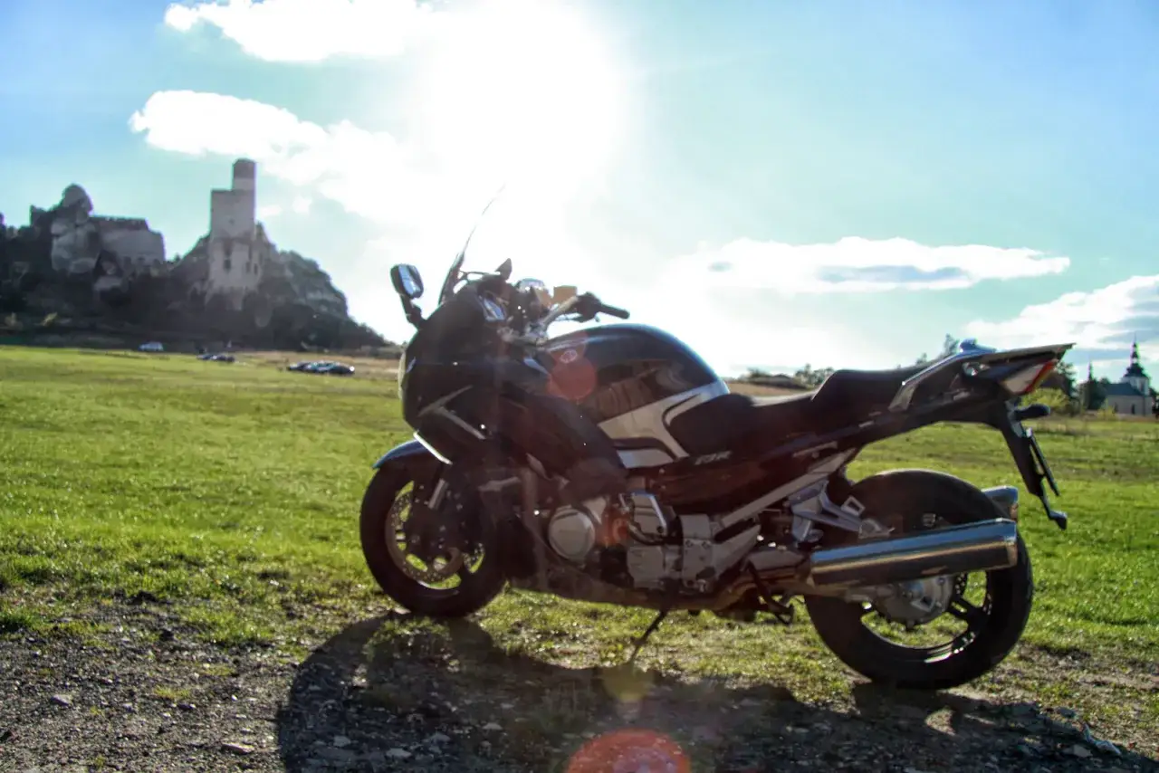 Motocykl na tle zamku na skale i zielonej łąki.