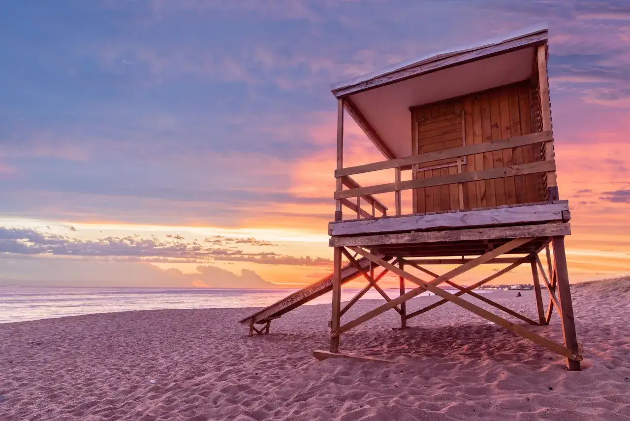 Drewniana wieża ratownicza na plaży o zachodzie słońca. Piasek i ocean tworzą tło dla tego malowniczego krajobrazu, który może być właśnie w Urugwaju, gdzie leży ten piękny kraj.
