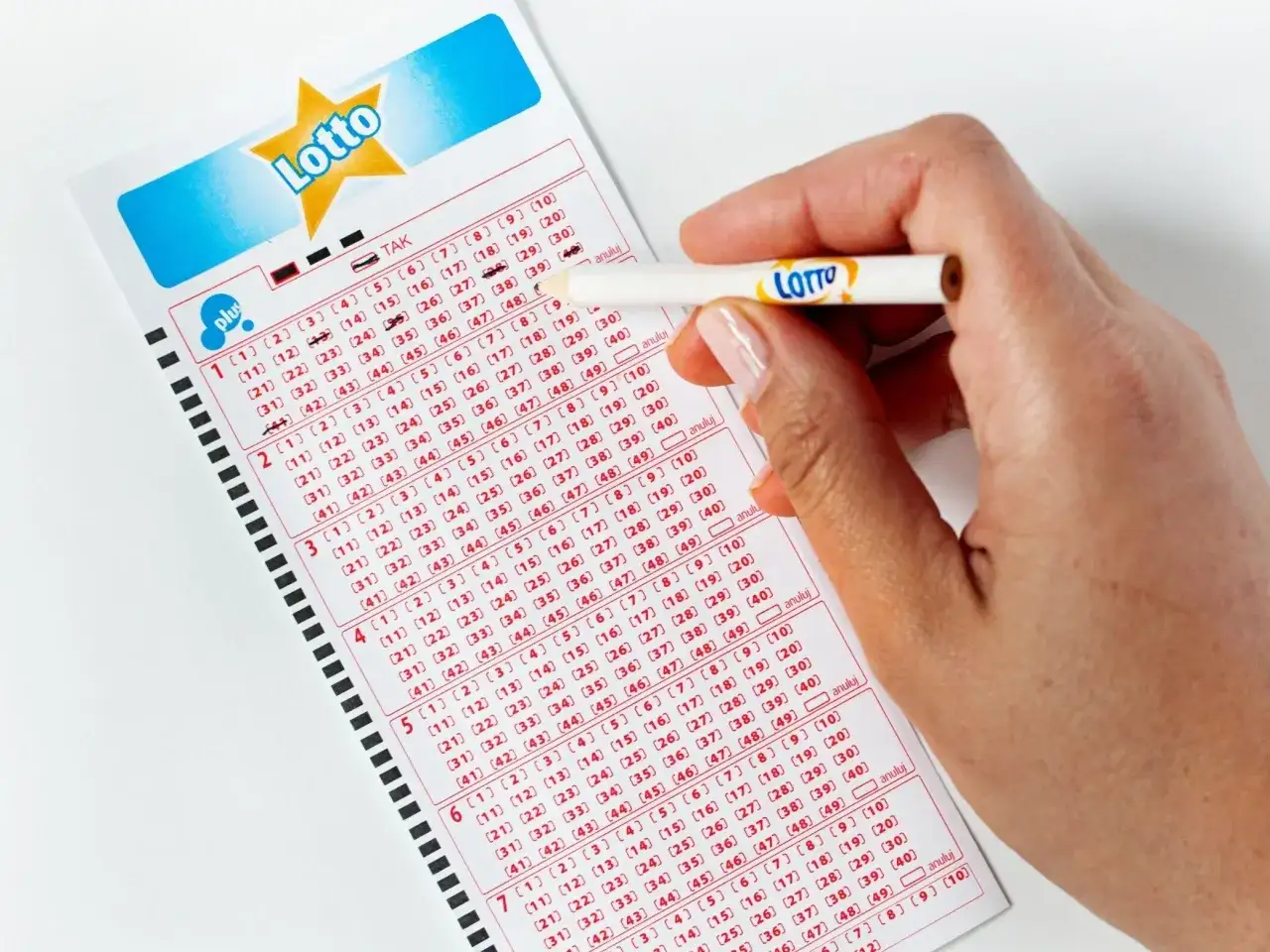Dłoń z ołówkiem Lotto zaznacza liczby na kuponie. Czy czwórka w Lotto Plus przyniesie szczęście?