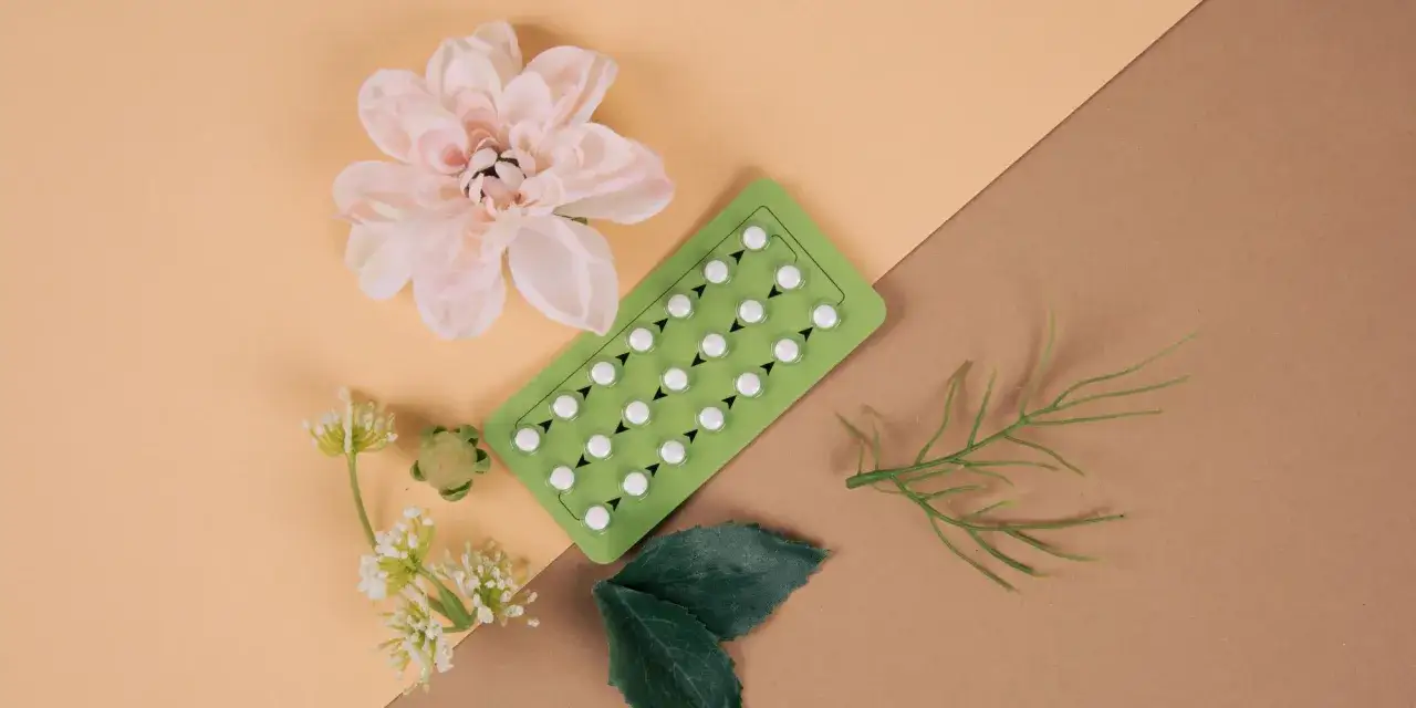 Pigułki antykoncepcyjne na zielonym blistrze, obok kwiatów i liści. Czy od tabletek antykoncepcyjnych się tyje?