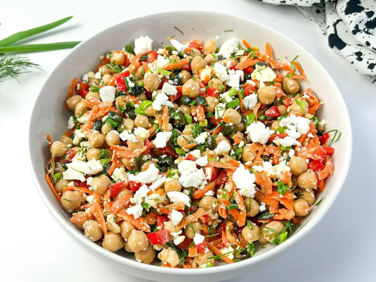 Kolorowy dodatek do sałatek: ciecierzyca, starta marchewka, papryka, ser feta i zioła w białej misce.