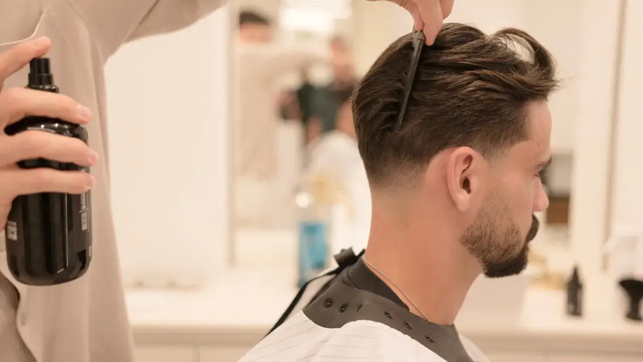 Stylista tworzy modną fryzurę dla mężczyzn, spryskując włosy i czesząc je grzebieniem.