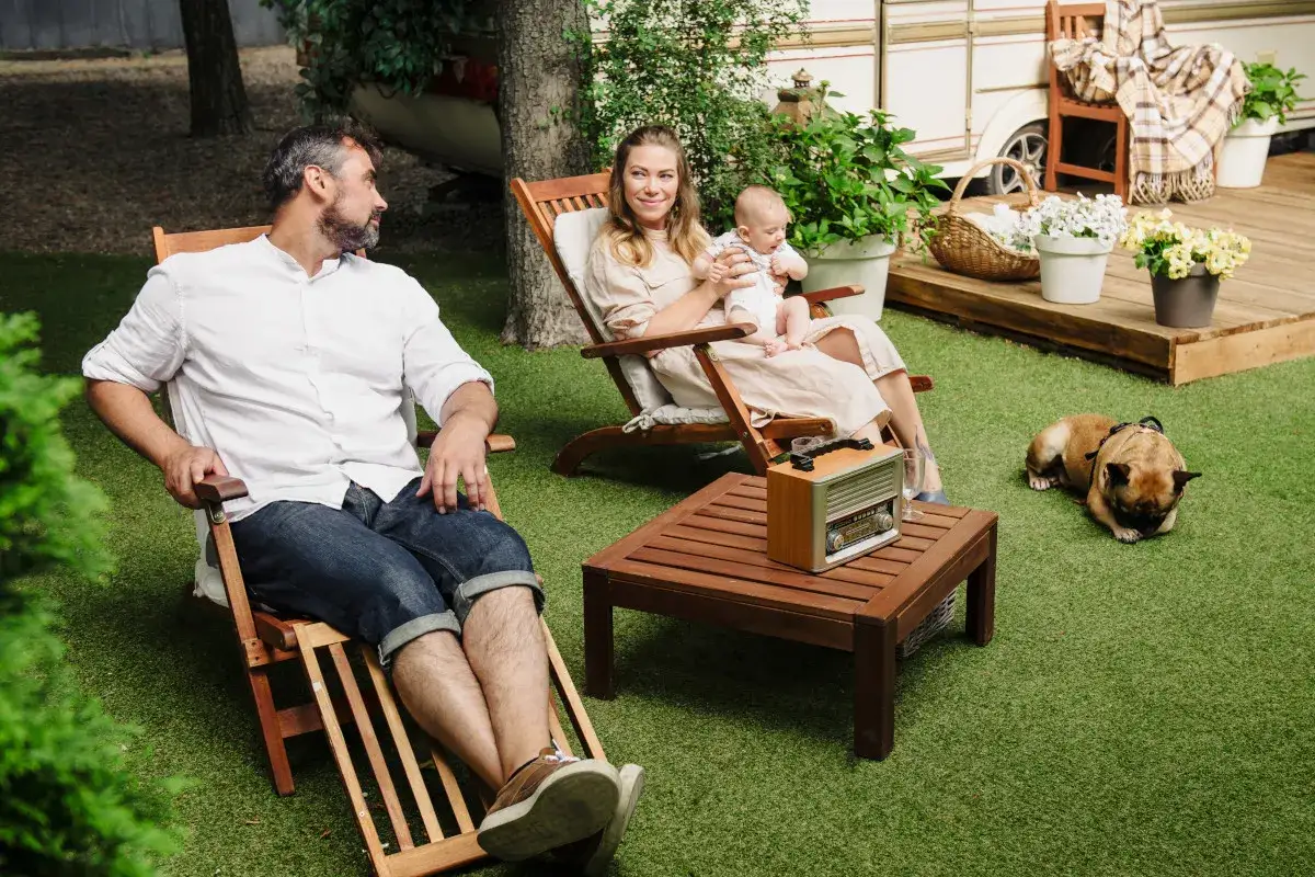 Rodzina cieszy się chwilą spokoju w swojej strefie relaksu w ogrodzie. Na trawniku leży piesek, a w tle widać kampera.