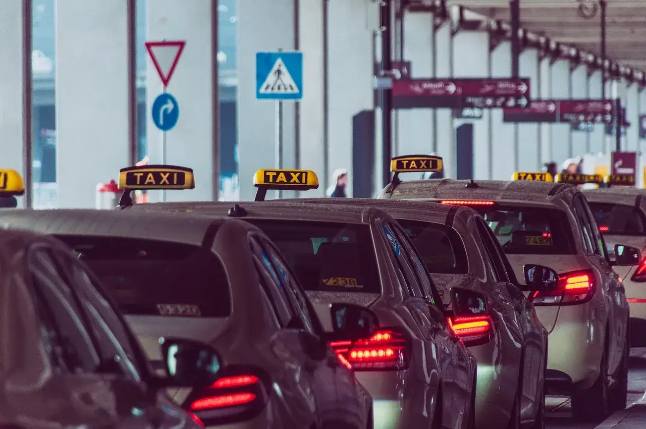 Rząd taksówek z żółtymi tabliczkami "TAXI" na dachu, stojących w kolejce.