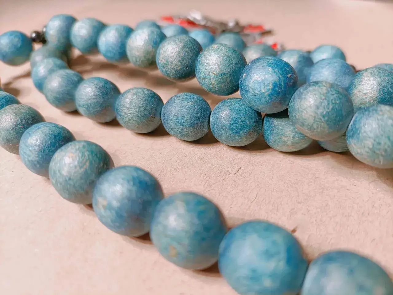 Niebieski, drewniany różaniec z widocznym krzyżykiem. Trudno określić, ile koralików ma różaniec, ale jest ich wiele, ułożonych w kilka rzędów.