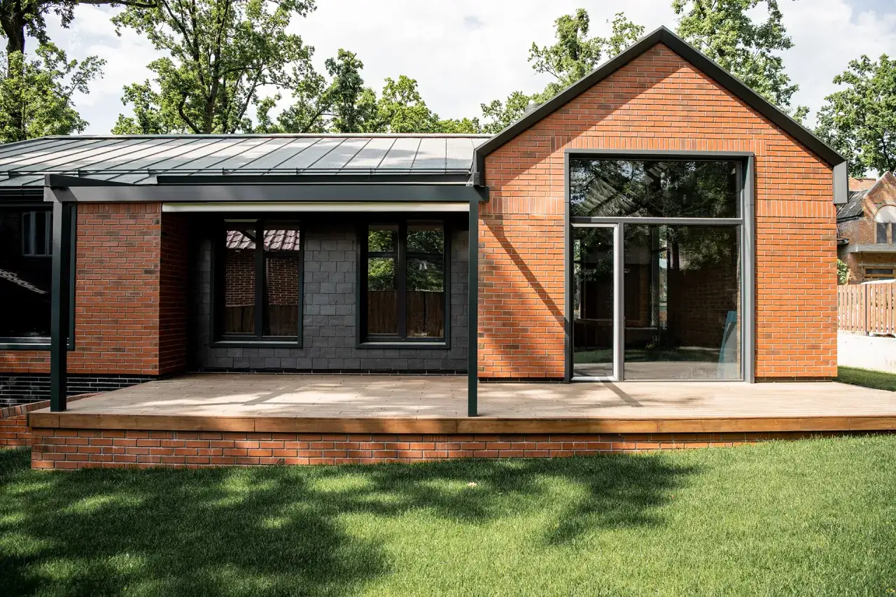 Nowoczesna budowa budynku mieszkalnego z cegły i ciemnej elewacji. Drewniany taras i duże okna.