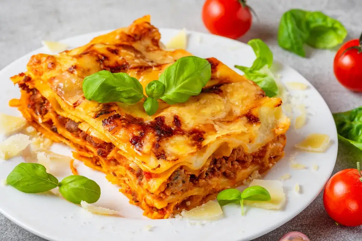 Pyszna, domowa lasagne jak z pieca, z warstwami makaronu, mięsa i sera, ozdobiona świeżą bazylią i parmezanem.