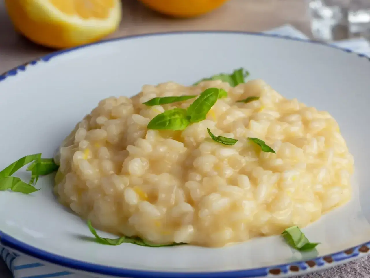 Kremowe risotto cytrynowe z bazylią na talerzu, w tle połówka cytryny.