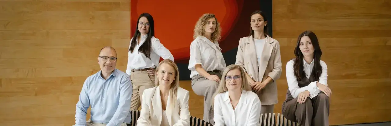 Grupa prawników w eleganckich strojach pozuje na tle drewnianej ściany i abstrakcyjnego obrazu.