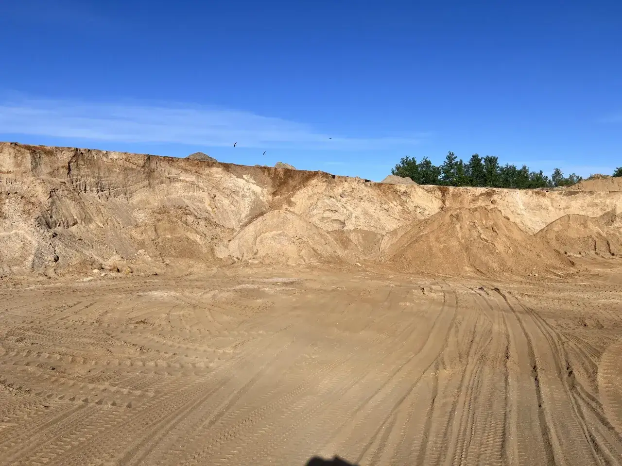 Piaskownia z usypiskami kruszywa i śladami opon pod błękitnym niebem.