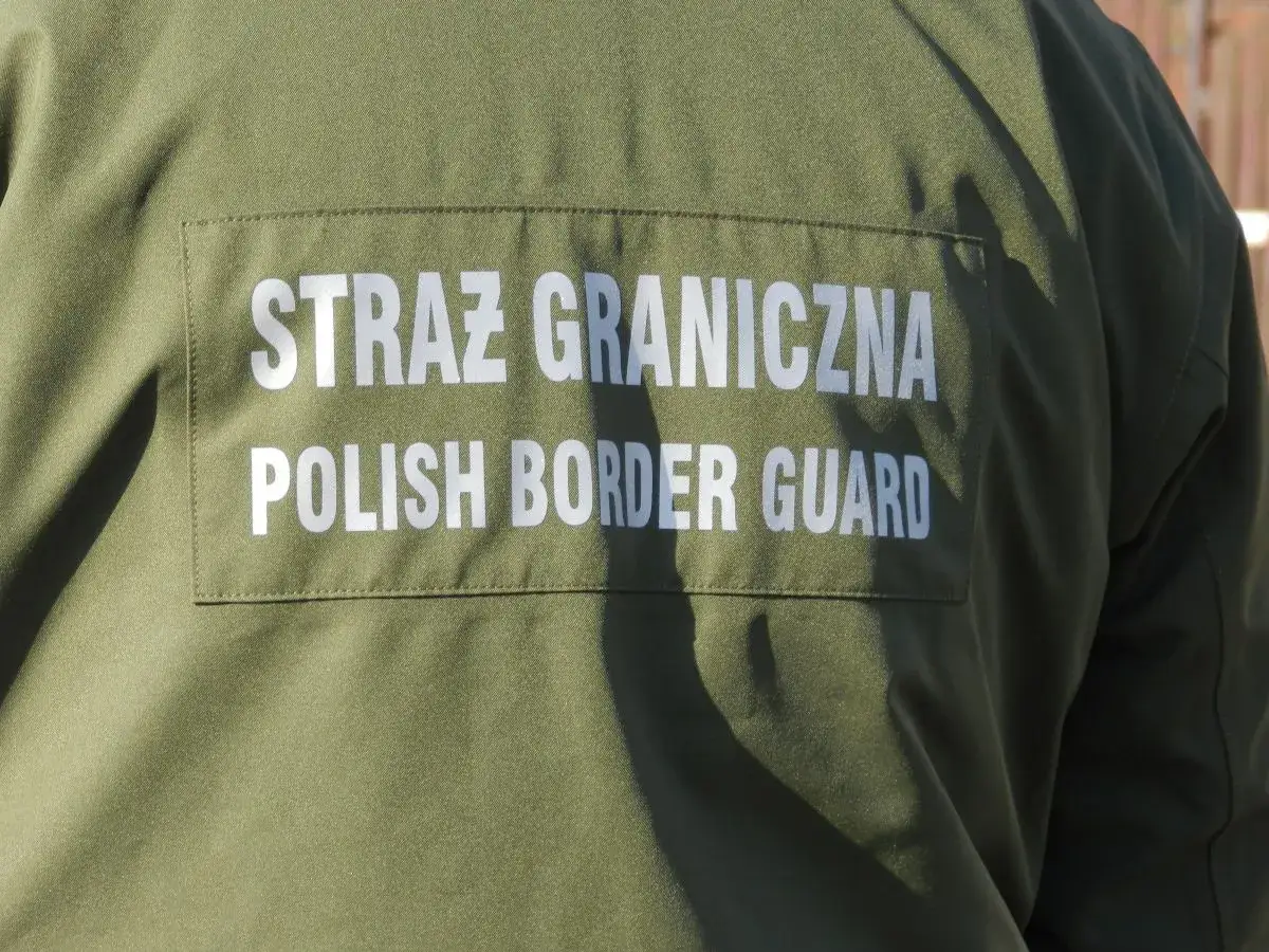 Fragment zielonego munduru Straży Granicznej z białym napisem "STRAŻ GRANICZNA POLISH BORDER GUARD".