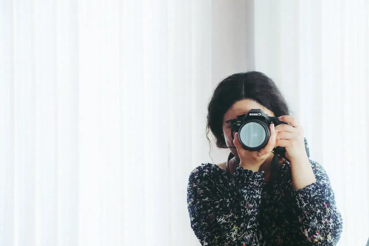 Kobieta z aparatem Canon, skupiona na kadrze. Rozwija swój biznes fotograficzny, łapiąc chwile.
