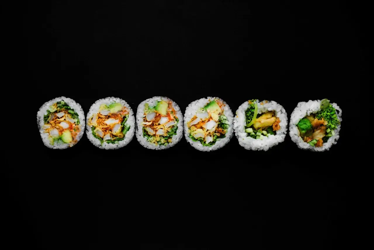 Sześć kawałków futomaki z awokado, kurczakiem i warzywami na czarnym tle.