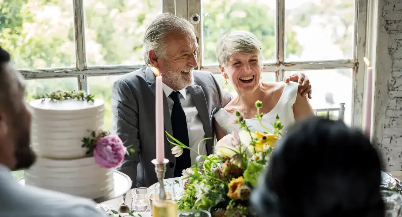 Szczęśliwa para świętuje 14 rocznicę ślubu. Uśmiechnięci, siedzą przy stole z tortem i kwiatami.
