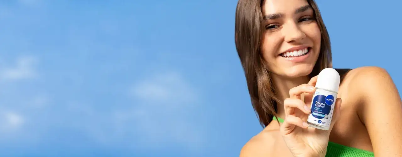 Uśmiechnięta kobieta trzymająca dezodorant Nivea Derma Control na tle błękitnego nieba.