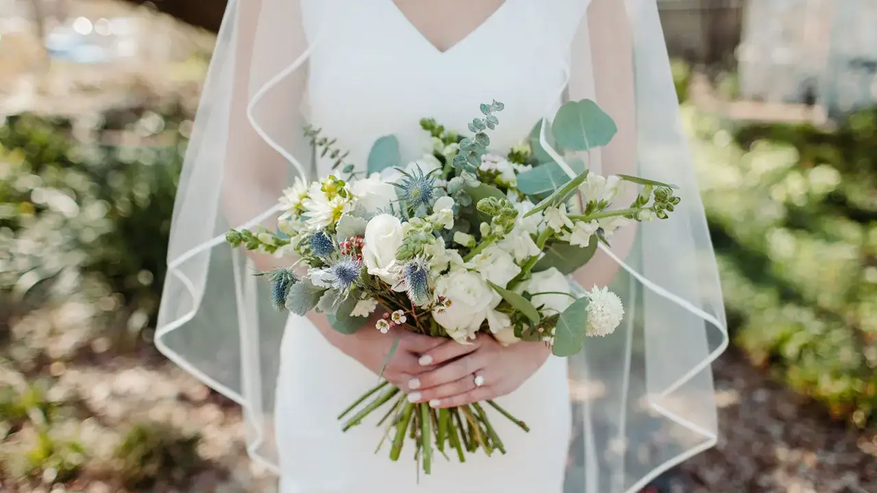 Panna młoda trzyma bukiet ślubny, w którym zastosowano technikę watowania we florystyce. Kwiaty są ułożone w luźny, naturalny sposób.