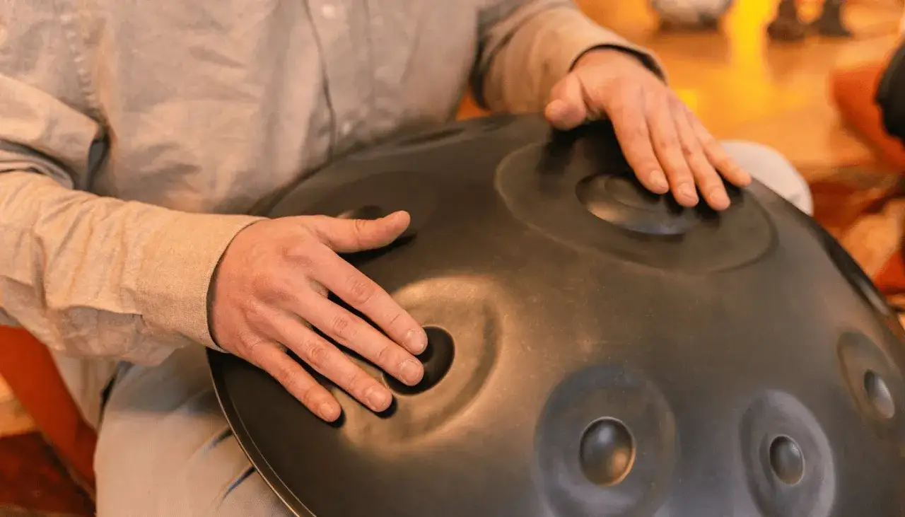 Dłonie grają na instrumencie typu hang drum, tworząc kojące dźwięki.