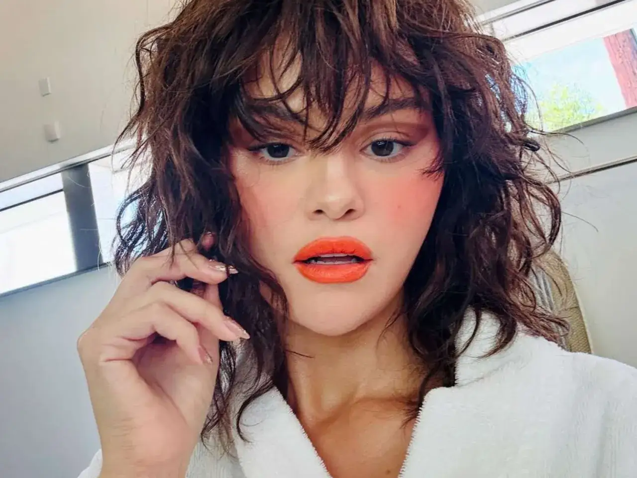 Selena Gomez w wolf cut, z pomarańczową szminką i różowymi policzkami. Fryzura pasuje do odważnych stylizacji.