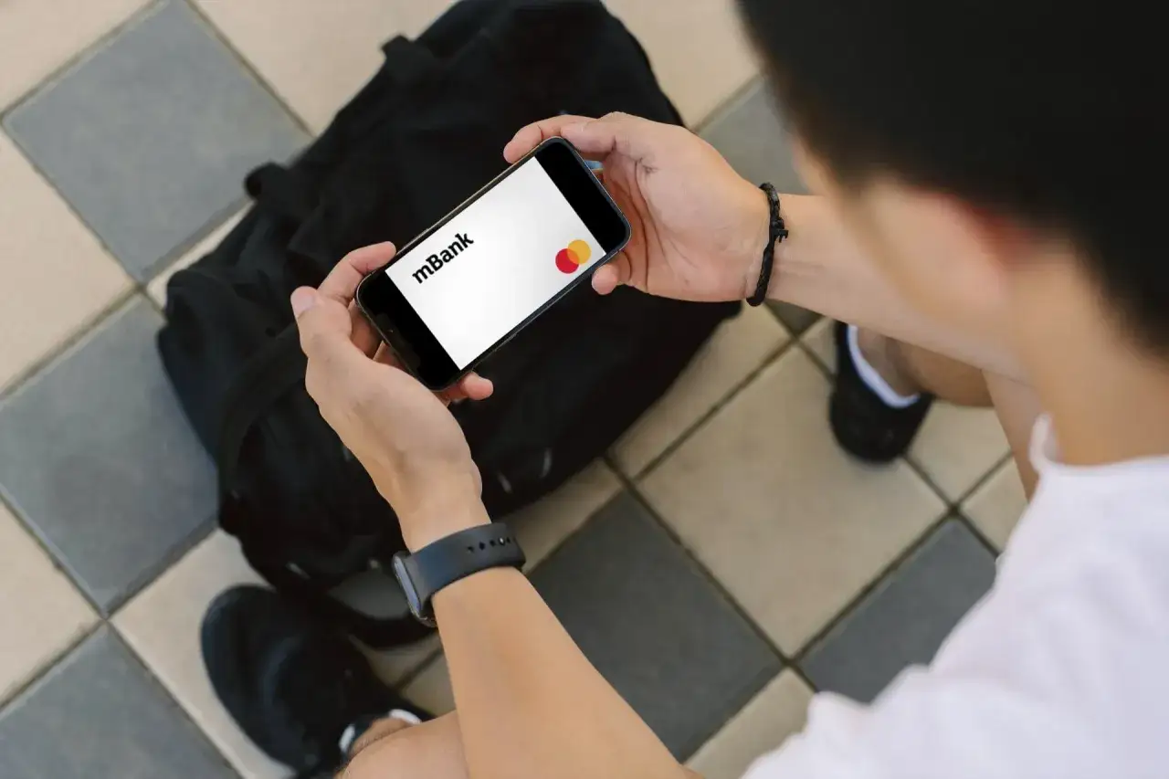Osoba trzyma smartfon z logo mBank i kartą Mastercard.
