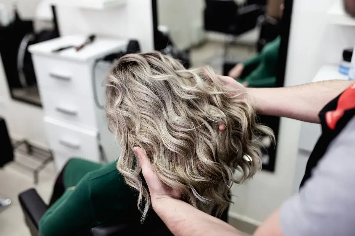 Profesjonalne usługi fryzjerskie: stylista układa falowane, blond włosy klientki w salonie.