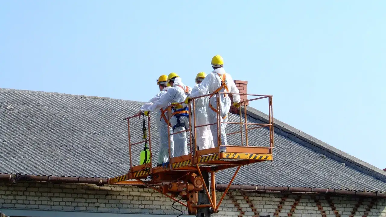 Pracownicy w kombinezonach na podnośniku przy dachu z eternitu. Zastanawiasz się, ile kosztuje usunięcie azbestu z dachu?