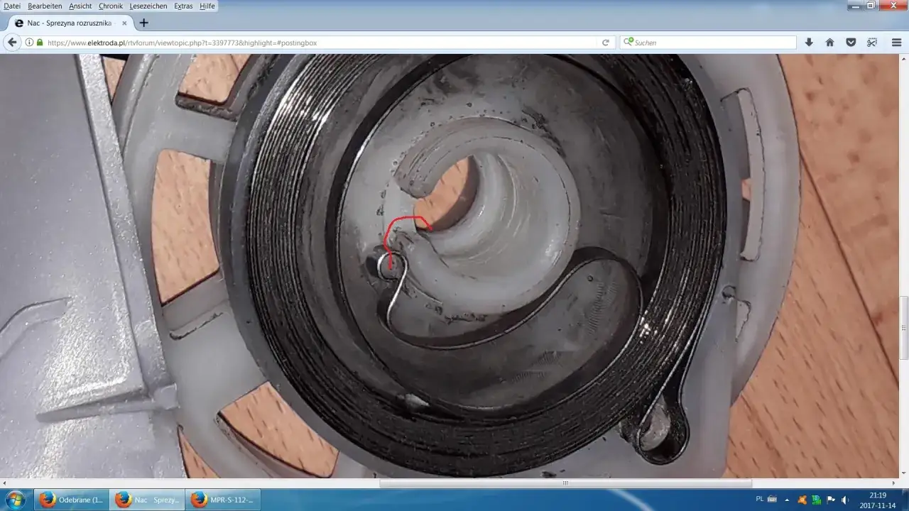 Szczegółowy widok mechanizmu szarpaka kosiarki, pokazujący jak założyć sprężynę do szarpaka kosiarki. Czerwony okrąg zaznacza punkt zaczepienia.