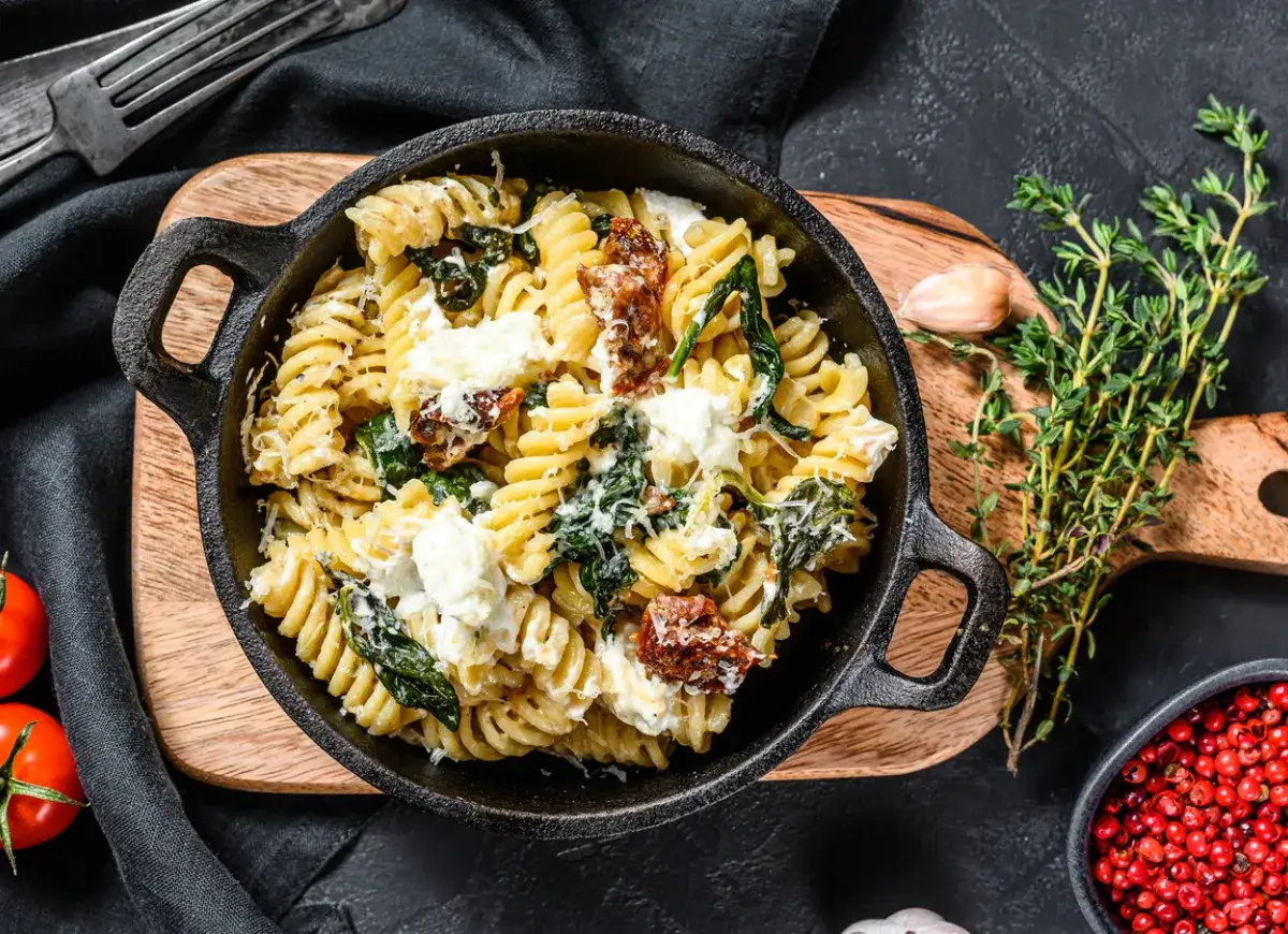 Pyszne fusilli ze szpinakiem i suszonymi pomidorami, posypane parmezanem i kawałkami sera feta.